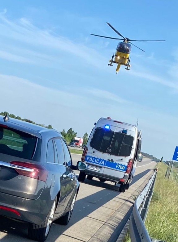 na zdjęciu oznakowany radiowóz, nad nim helikopter lotniczego pogotowia ratunkowego, autostrada.