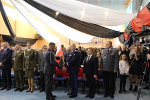 Symboliczne przekazywani flagi państwowej przez zaproszonych gości. Na pierwszym planie Komendant Wojewódzki odbiera flagę od przedstawiciela wojska.
