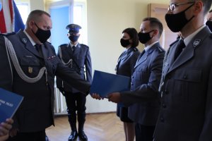 Komendant gratuluje awansu policjantowi, w tle inni awansowani oraz poczet sztandarowy.