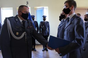 Komendant gratuluje awansu policjantowi, w tle inni awansowani oraz poczet sztandarowy.