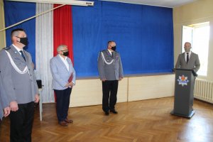 Po prawej stronie zdjęcia przy mównicy Pan Robert Szczepanik reprezentujący Starostwo Powiatowe w Łasku gratuluje awansowanym. Po lewej stronie zdjęcia stoi policjant, Burmistrz Łasku oraz Komendant.