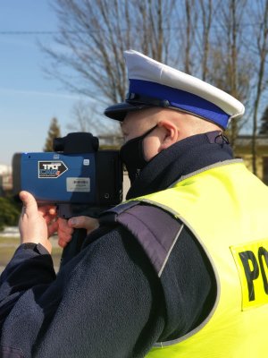 W przybliżeniu widać lewy profil umundurowanego policjanta Wydziału Ruchu Drogowego dokonującego pomiaru z urządzenia TruCAM.