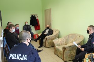 W pomieszczeniu biurowym dwóch umundurowanych policjantów prowadzi szkolenie z pracownikami Zakładu Komunikacji Miejskiej. Wszyscy siedzą na krzesłach rozmieszczonych w okręgu z zachowaniem zasad reżimu sanitarnego.
