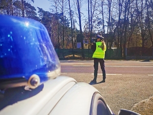 Na zdjęciu znadjuje się policjantka, która stoi przy drodze i mierzy prędkość.
