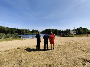 Policjant, strażak i ratownik WOPR stoją przed plaża na kąpielisku miejskim i obserwują brzeg wody.