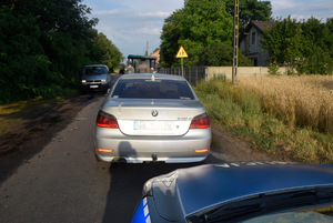 Na drodze stoi kolejno ciągnik wraz z kierującym, samochód marki BMW oraz policyjny radiowóz.