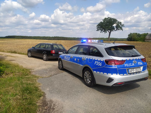 Policyjny radiowóz na włączonych światłach stoi za zatrzymanym pojazdem marki Audi.