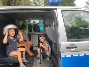 Czwórka dzieci siedzi w policyjnym radiowozie, dzieci mają ubrane elementy policyjnego wyposarzenia.