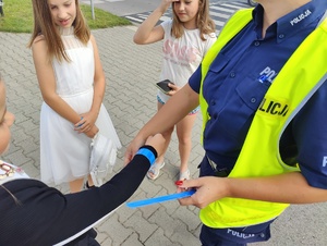 Policjantka wręcza dzieciom opaski odblaskowe.