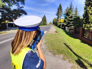 Policjantka ruchu drogowego mierzy prędkość pojazdów w rejonie przejścia dla pieszych.