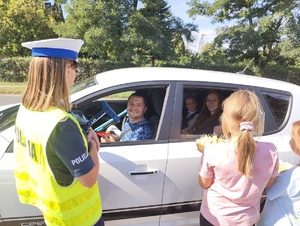 Policjantka wraz z dziewczynkami wręcza jabłko kierującemu za przepisową jazdę. Kierujący uśmiecha się.