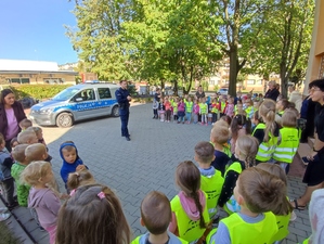 Policjant stoi przed przedszkolakami i opowiada o bezpiecznych zachowaniach na drodze.