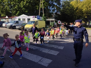 Policjant przeprowadza dzieci przez przejście dla pieszych.
