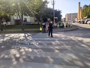 Policjant zatrzymuje ruch aby dzieci mogły bezpiecznie przejść przez drogę.