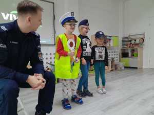 Policjant pozuje do zdjęcia z przedszkolakami ubranymi w czapki policyjne.