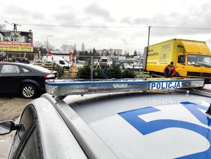 Policyjny radiowóz stoi przy punkcie sprzedaży choinek.