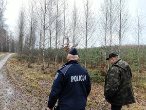 Policjant wraz z stażnikiem leśnym kontroluje pieszo teren leśny.