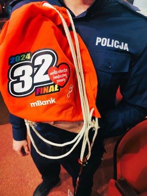 Policjant trzyma worek 32 finalu Wielkiej Orkiestry Świątecznej Pomocy.