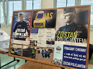 Na tablicy informacyjnej wiszą ulotki promujące zawód policjanta.