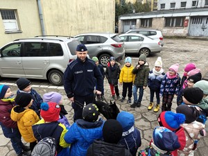 Policjant opowiada zebranym wkoło niego dzieciom o pracy policyjnego przewodnika psa.