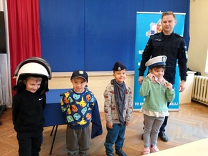 Policjant wraz z dziećmi pozuje do zdjęcia. Dzieci mają założone policyjne czapki.