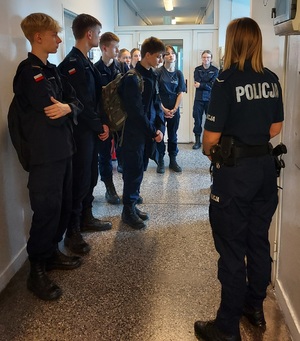 Policjanta stojąca tyłem. Z prawej strony uczniowie klasy mundurowej.