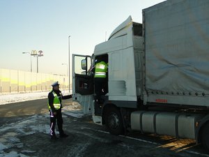 Policjant wraz z funkcjonariuszem Inspektoratu Transporu Drogowego kontroluje pojazd ciężarowy.