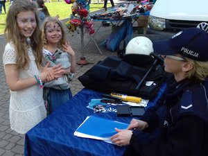 Policjantka rozmawia z dziewczynkami o bezpieczeństwie na stoisku plenerowym.