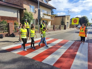 Policjanci z dziecmi przechodzą przez przejście dla pieszych.