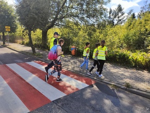 Policjant z dziecmi przechodzą przez przejście dla pieszych.