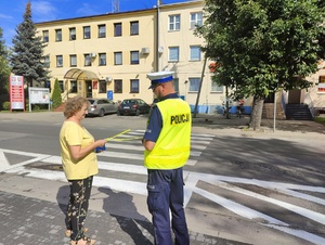 Policjant wręcza opaskę odblaskową kobiecie.