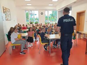 Polcjant stoi przed grupą dzieci i opowiada o bezpieczeństwie nad wodą.