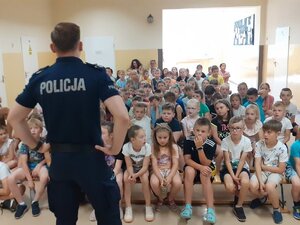 Policjant stoi przed grupą uczniów i opowiada o bezpieczeństwie.