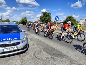 Obok stojącego na skrzyżowaniu radiowozu przejeżdza peleton kolarzy.