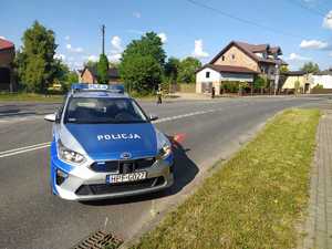 Na skrzyżowaniu dróg wojewódzkich stoi policjanta Wydziału Ruchu Drogowego i kieruje ruchem. Na pierwszym plasnie stoi radiozwóz policyjny.