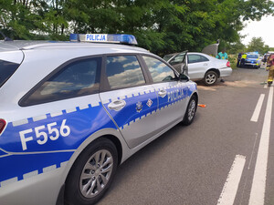 Policjanci wykonują czynności na miejscu zdarzenia drogowego. Pojazd marki mercedes stoi częściowo na drodze a częsciowo w rowie.