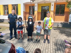 Policjant wraz z czwórką dzieci pozuje do zdjęcia. Dzieci mają na sobie elementy policyjnego ubioru.