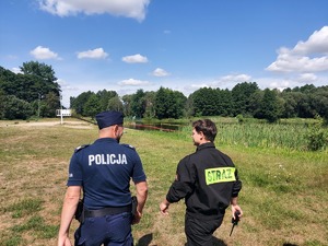 Policjant wraz ze strażakiem kontrolują brzeg kąpieliska miejskiego w Łasku.