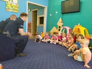 Policjanci rozmawiają z dziecmi o bezpieczeństwie. Dzieci siedzą na dywanie przed policjantami.