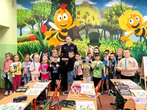 Pierwszoklasiści wraz z policjantem pozują do zdjęcia grupowego. Dzieci trzymają w rękach opaski odblaskowe.