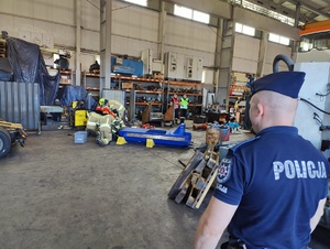 Policjant zabezpiecza miejsce zdarzenia na hali produkcyjnej.