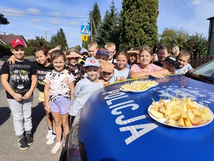 Dzieci stoją orzy policyjnym aucie i pozują do zdjęcia.