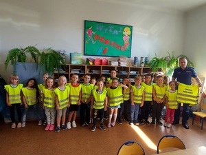 Policjant pozuje do zdjęcia grupowego z dziećmi ubranymi w kamizelki odblaskowe.