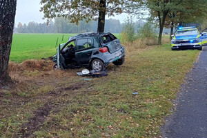 Zniszczona kombletnie toyota po uderzeniu w drzewo. W tle policyjny radiowóz.
