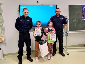 Policjanci wraz z dziećmi pozują do zdjęcia. Dzieci trzymają w dłoniach nagrody.