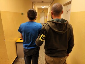 Policjant trzyma zatrzymanego za rękę.