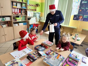 Policjant rozdaje dzieciom siedzącym w łace odblaski.