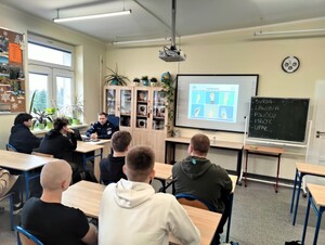 Policjant rozmawia z młodzieżą o uzależnianiach. Na ekranie projektora wyświetla się napisa uzależnienia.