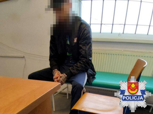 Na ławce siedzi zatrzymany mężczyzna. Ma założone kajdanki na ręce.