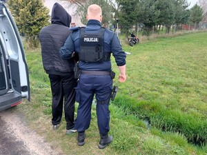 Policjant trzyma pod rękę zatrzymanego mężczyznę. W tle widać odzyskany motorower.